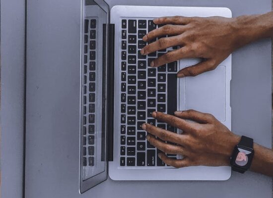 Top view of hands typing on a laptop beside a mask and smartphone.